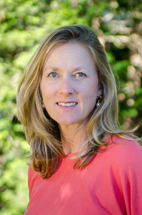 A woman in a pink shirt is smiling for the camera.
