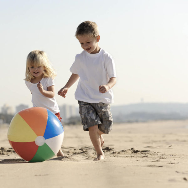 Two children playing with a ball on the beach.