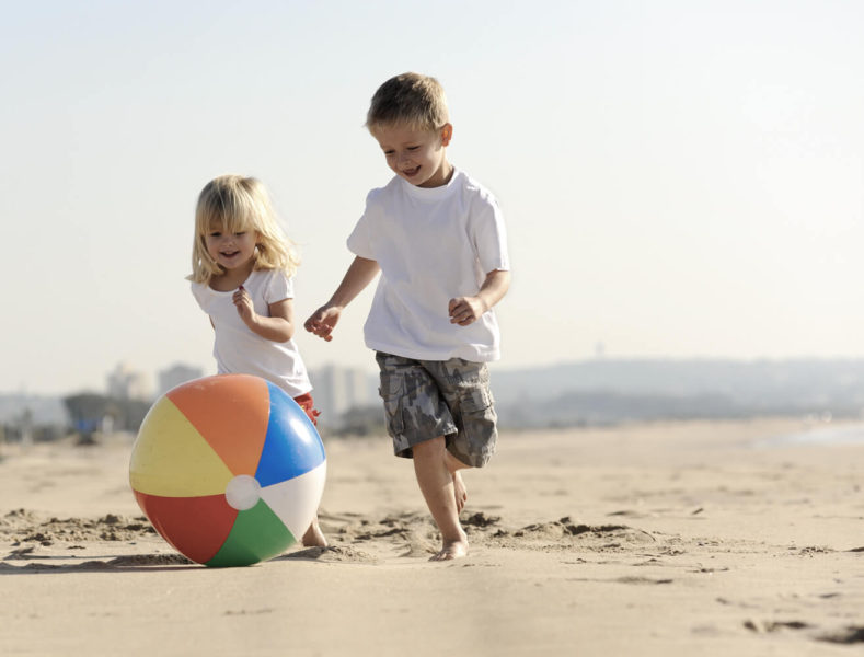 Two children playing with a ball on the beach.