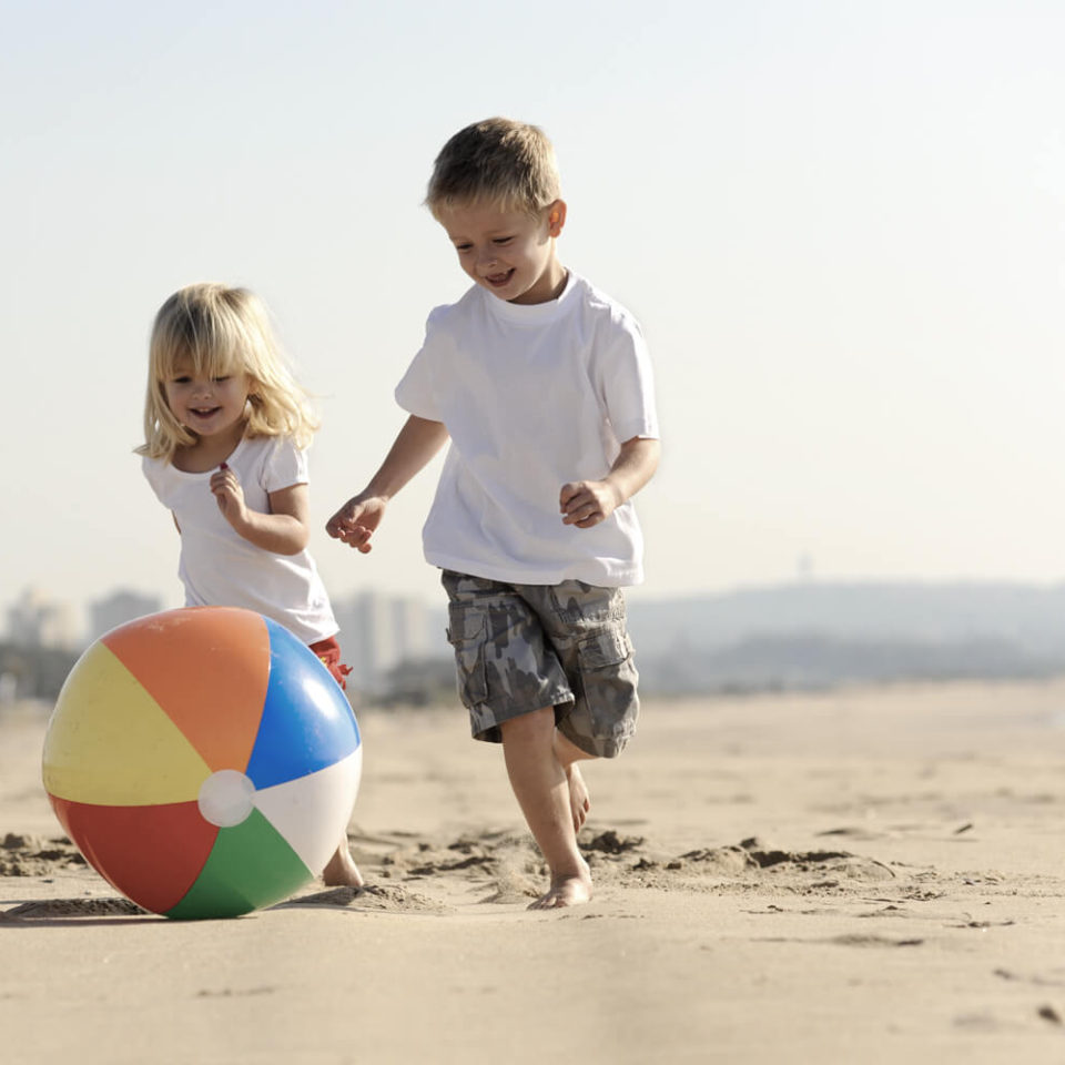 Two children playing with a ball on the beach.