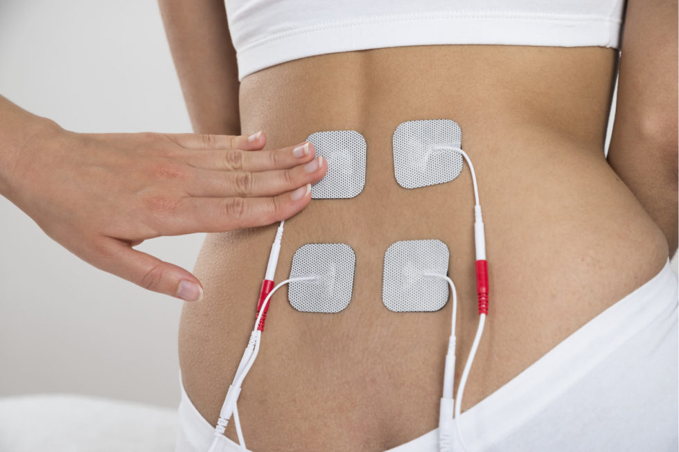 A woman is holding four electrodes on her back.